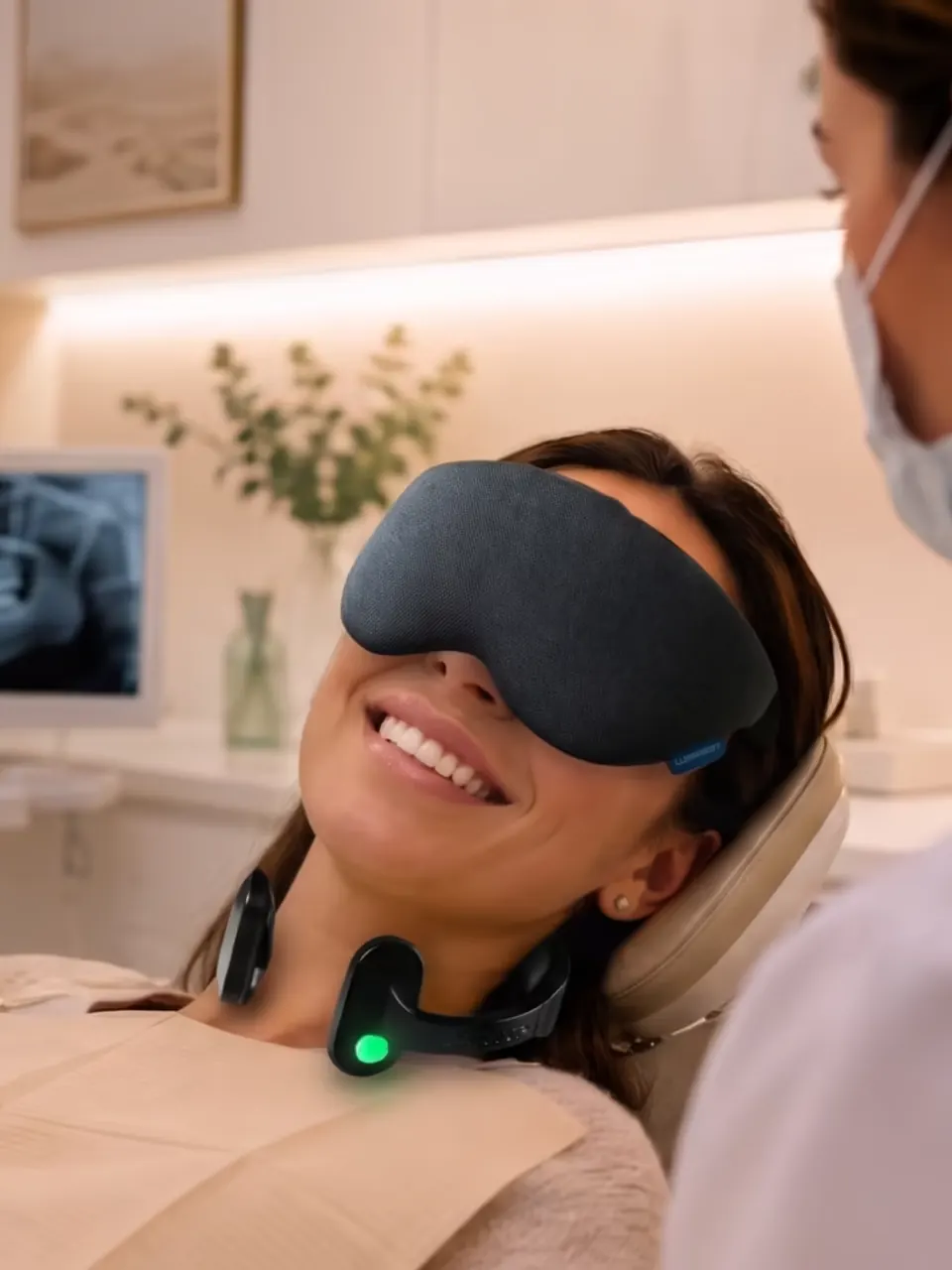 A smiling patient relaxing in the treatment chair with an eye mask and a calming neck device
